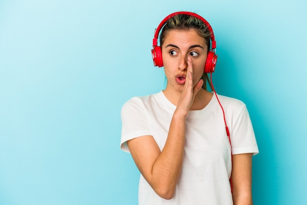 La giovane donna bionda che ascolta la musica sulle cuffie isolate su priorità bassa blu sta dicendo una notizia di frenata calda segreta e sta guardando da parte