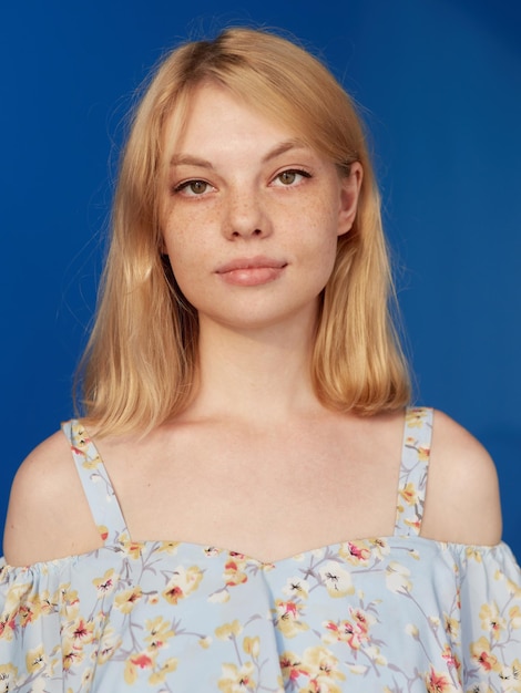 La giovane donna bionda con i capelli biondi ha la lentiggine che esamina la priorità bassa blu isolata della macchina fotografica