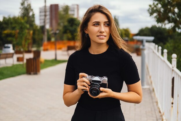 La giovane donna bionda prova un hobby fotografico con una macchina fotografica d'epoca all'aperto