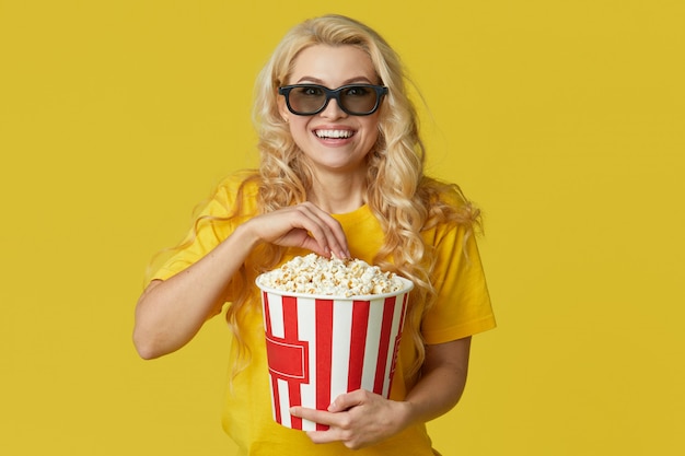 La giovane donna bionda sorpresa in vetri 3d e la camicia gialla che mangiano il popcorn, sembra il film scioccante al cinema. Isolato