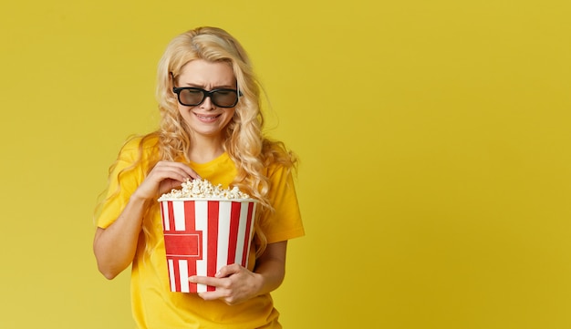 La giovane donna bionda sorpresa in vetri 3d e la camicia gialla che mangiano il popcorn, sembra il film scioccante al cinema. Isolato