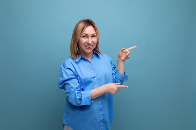 La giovane donna bionda sorridente in camicia casual mostra le mani a destra su un baner su sfondo blu