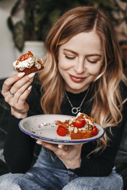 La giovane donna bionda sta mangiando il toast dell'avocado per colazione in un caffè.