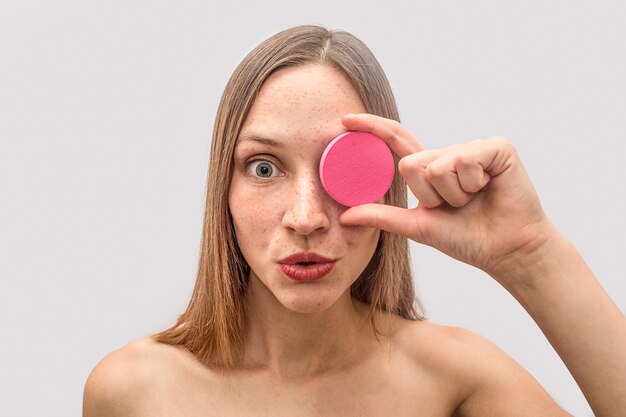 La giovane donna bionda tiene la spugna rosa e copre l'occhio di esso. È stupita e meravigliata. La modella sembra.