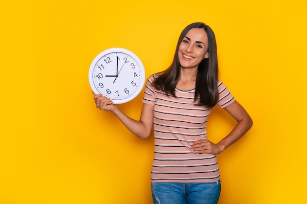 La giovane donna carina e attraente con un grande orologio bianco in mano mostra questo sulla fotocamera