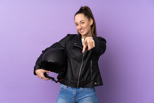 La giovane donna castana con un casco del motociclo sopra la parete porpora isolata indica il dito con un'espressione sicura