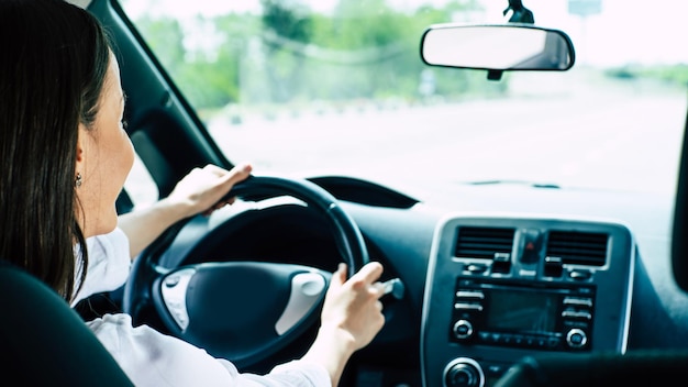 La giovane donna castana felice sveglia di successo sta guidando un'auto. Dopo la concessionaria. Auto da lavoro. Veicolo del futuro