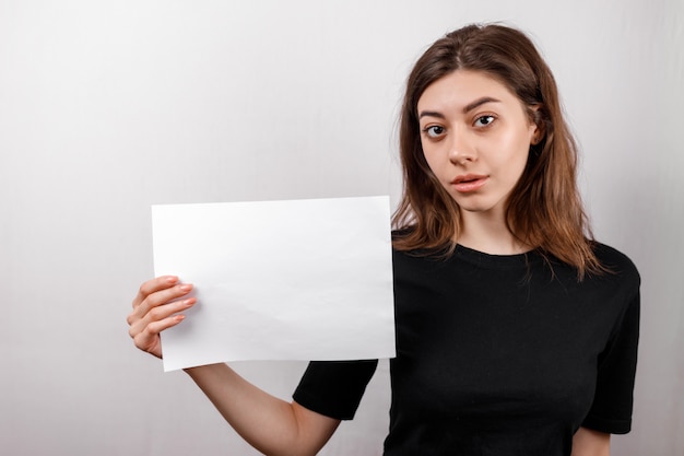 La giovane donna castana in una maglietta nera che sorride mostra uno strato bianco su uno spazio bianco. copyspase