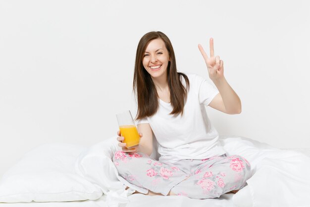 La giovane donna castana si siede sul letto con il lenzuolo bianco, cuscino, avvolgente in una coperta isolata sul muro bianco