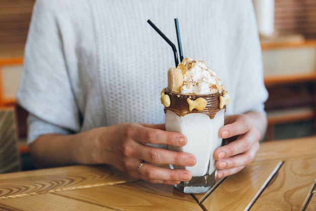 La giovane donna castana sveglia beve il frappè splendidamente decorato con crema e biscotti nella caffetteria. Tonificante.