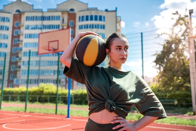 La giovane donna caucasica abbastanza sportiva tiene la pallacanestro sul campo da pallacanestro