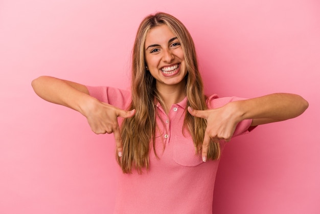 La giovane donna caucasica bionda isolata sulla parete rosa punta verso il basso con le dita, sensazione positiva