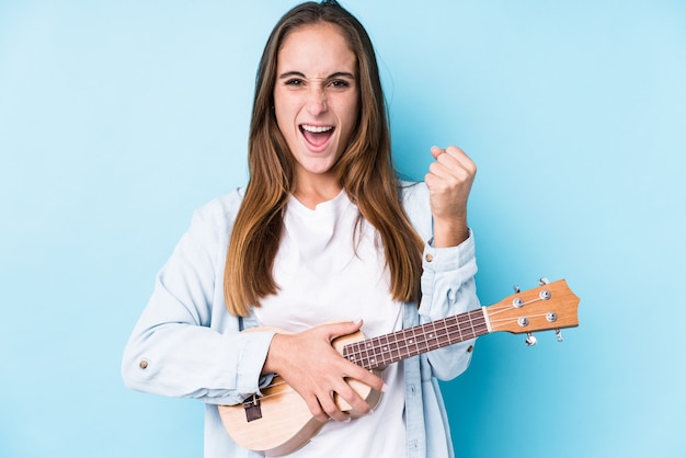 La giovane donna caucasica che giudica un ukelele ha isolato incoraggiare spensierato ed eccitato. Concetto di vittoria.