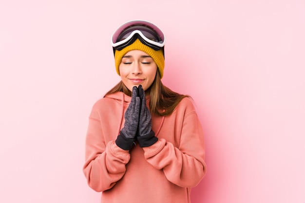 La giovane donna caucasica che indossa i vestiti di uno sci che tengono le mani dentro prega vicino alla bocca, si sente sicura.