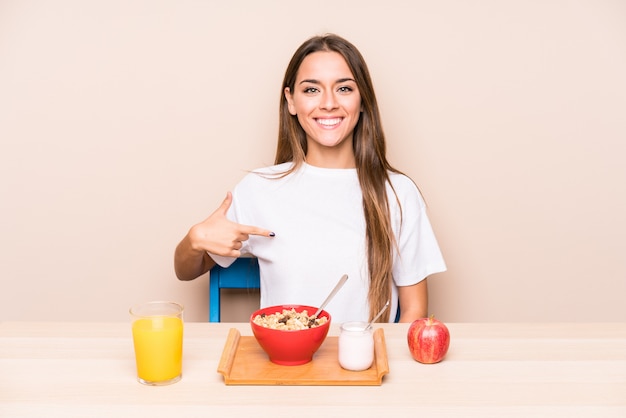 La giovane donna caucasica che mangia una prima colazione ha isolato la persona che indica a mano uno spazio della copia della camicia, fiero e sicuro