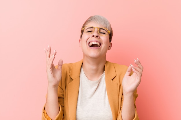 La giovane donna caucasica che porta un commercio casuale copre ridere allegro molto. Concetto di felicità.