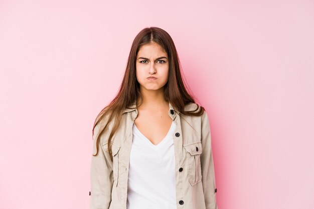 La giovane donna caucasica che posa in un muro rosa soffia sulle guance, ha un'espressione stanca. Concetto di espressione facciale.