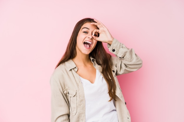 La giovane donna caucasica che posa in una parete rosa ha eccitato mantenendo il gesto giusto sull'occhio.