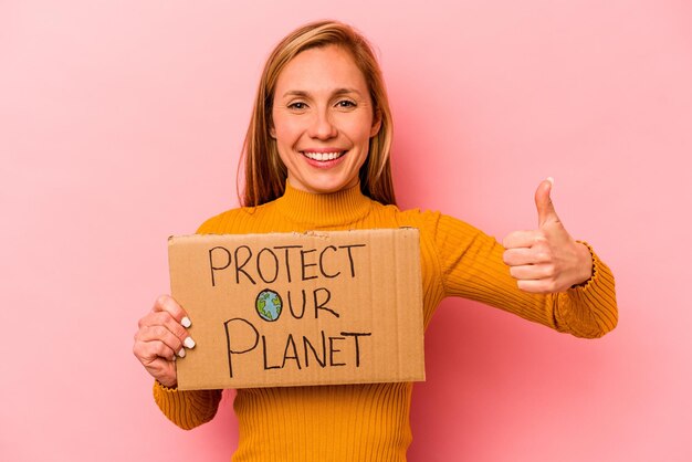 La giovane donna caucasica che tiene protegge il nostro pianeta cartello isolato su sfondo rosa