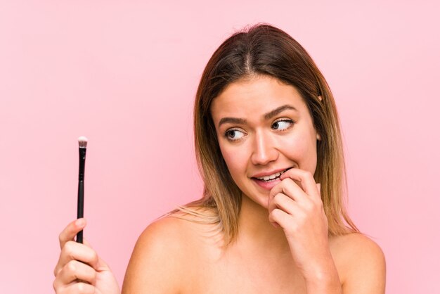 La giovane donna caucasica che tiene un eyebrush si è distesa pensando a qualcosa