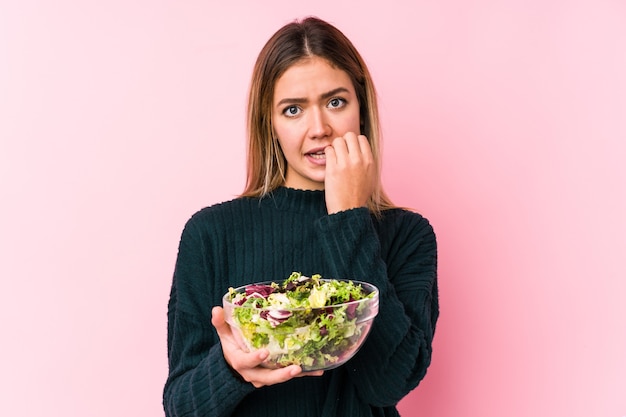 La giovane donna caucasica che tiene un'unghia mordace isolata insalata, nervosa e molto ansiosa.