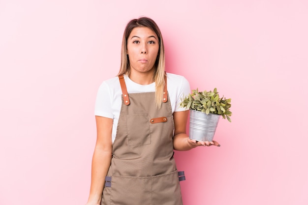 La giovane donna caucasica del giardiniere ha isolato le spalle di scrollate di spalle e gli occhi aperti confusi.