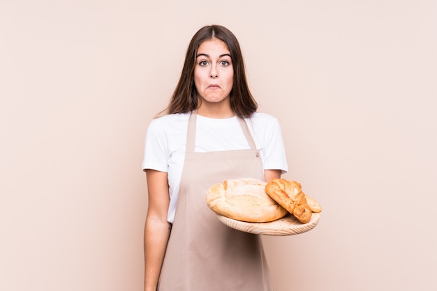 La giovane donna caucasica del panettiere ha isolato le spalle di scrollate di spalle e gli occhi aperti confusi.