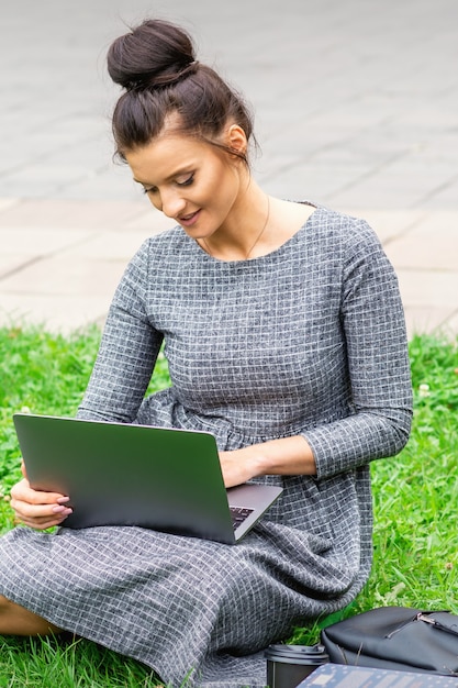 La giovane donna caucasica dell'allievo utilizza il computer portatile che si siede sull'erba sulla strada