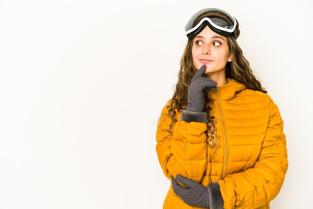 La giovane donna caucasica dello snowboarder ha isolato che osserva obliquamente con l'espressione dubbiosa e scettica.