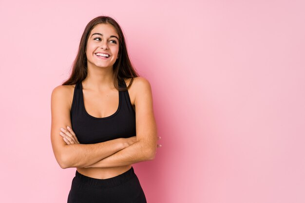 La giovane donna caucasica di forma fisica che fa lo sport ha isolato sorridere sicuro con le armi attraversate.