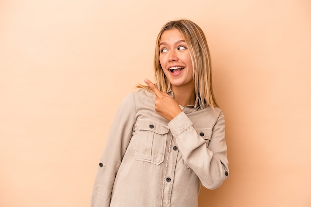 La giovane donna caucasica isolata su fondo beige guarda da parte sorridente, allegra e piacevole.