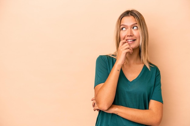 La giovane donna caucasica isolata su fondo beige si è rilassata pensando a qualcosa guardando uno spazio di copia.