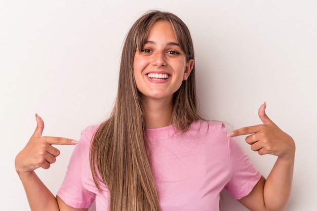 La giovane donna caucasica isolata su fondo bianco indica con le dita, sensazione positiva.