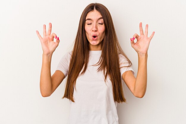 La giovane donna caucasica isolata su fondo bianco si rilassa dopo una dura giornata di lavoro, sta eseguendo lo yoga.