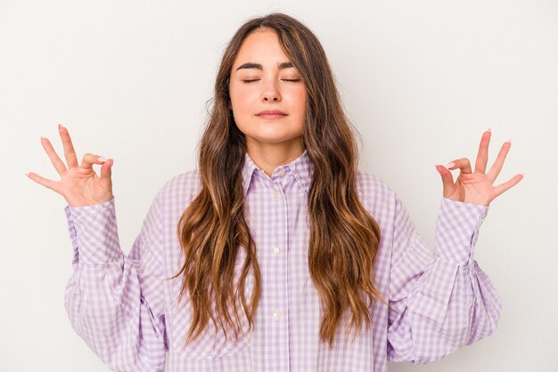 La giovane donna caucasica isolata su fondo bianco si rilassa dopo una dura giornata di lavoro, sta eseguendo lo yoga.