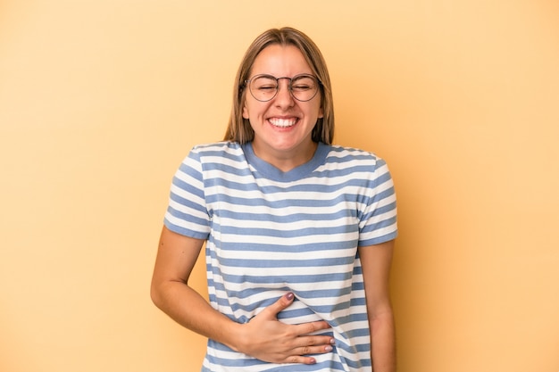 La giovane donna caucasica isolata su fondo giallo tocca la pancia, sorride dolcemente, mangia e concetto di soddisfazione.