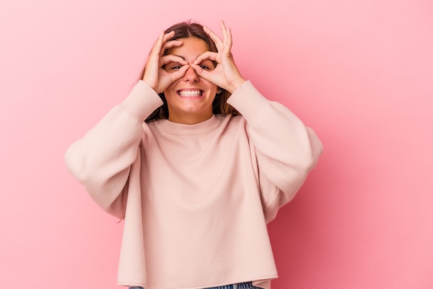 La giovane donna caucasica isolata su fondo rosa ha eccitato mantenendo il gesto giusto sull'occhio.