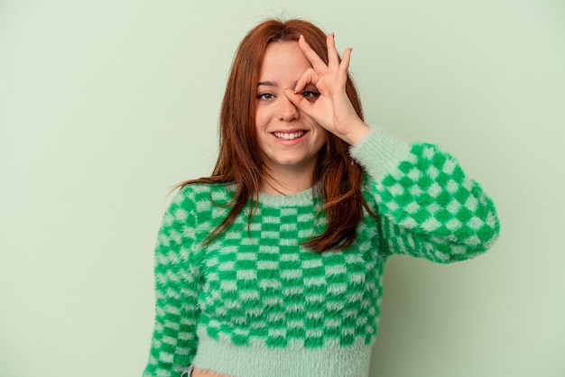 La giovane donna caucasica isolata su fondo verde ha eccitato mantenendo il gesto giusto sull'occhio.