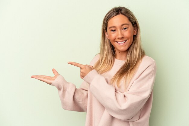 La giovane donna caucasica isolata su fondo verde ha eccitato tenendo uno spazio della copia sulla palma.