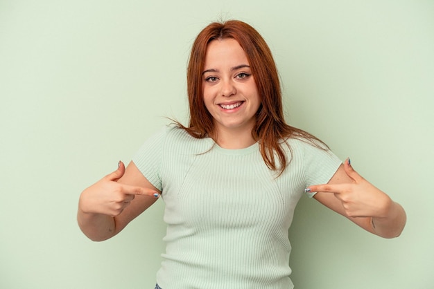 La giovane donna caucasica isolata su fondo verde indica con le dita, sensazione positiva.