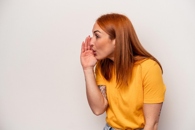 La giovane donna caucasica isolata su sfondo bianco sta dicendo una notizia segreta di frenata calda e sta guardando da parte