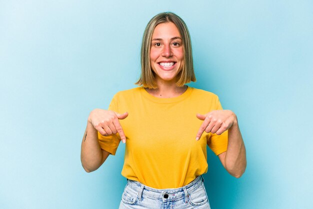 La giovane donna caucasica isolata su sfondo blu indica con le dita una sensazione positiva