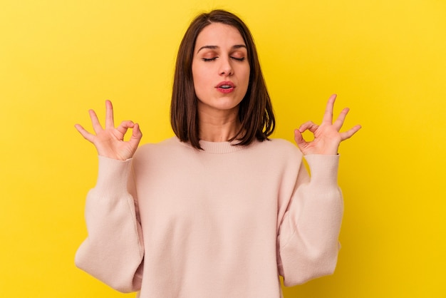 La giovane donna caucasica isolata su sfondo giallo si rilassa dopo una dura giornata di lavoro, sta eseguendo yoga.