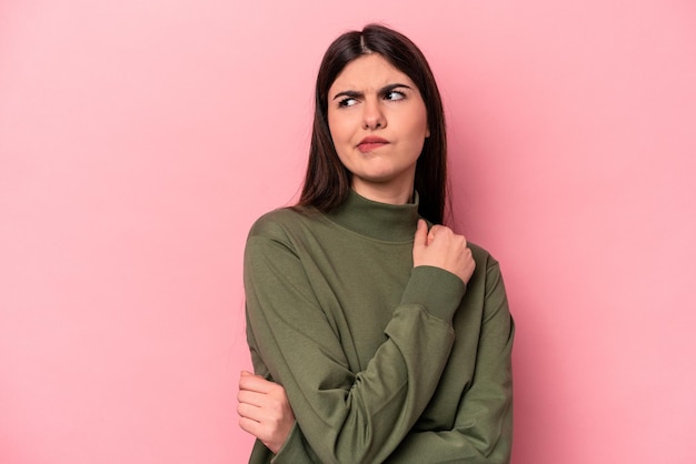 La giovane donna caucasica isolata su sfondo rosa confusa si sente dubbiosa e insicura