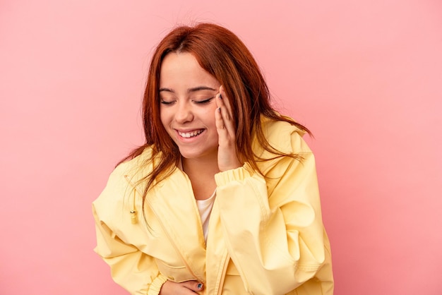 La giovane donna caucasica isolata su sfondo rosa ride allegramente e si diverte a tenere le mani sullo stomaco.