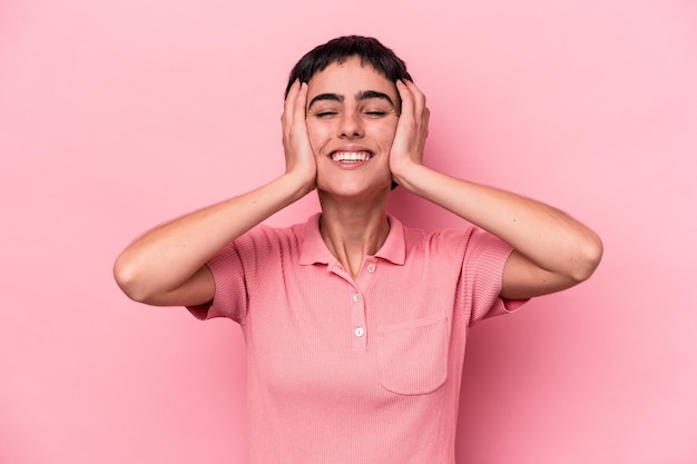 La giovane donna caucasica isolata su sfondo rosa ride con gioia tenendo le mani sulla testa. Concetto di felicità.