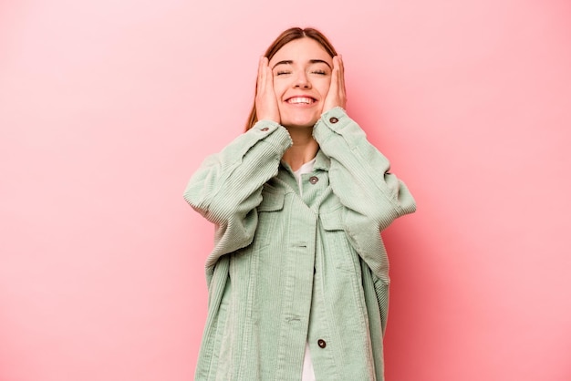 La giovane donna caucasica isolata su sfondo rosa ride con gioia tenendo le mani sulla testa Concetto di felicità