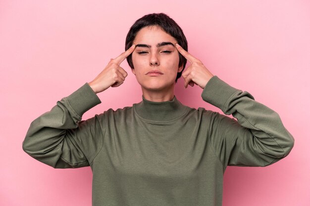 La giovane donna caucasica isolata su sfondo rosa si è concentrata su un compito, tenendo gli indici rivolti verso la testa.