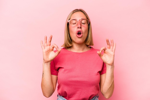 La giovane donna caucasica isolata su sfondo rosa si rilassa dopo una dura giornata di lavoro che sta eseguendo yoga