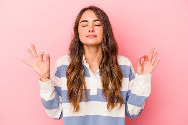 La giovane donna caucasica isolata su sfondo rosa si rilassa dopo una dura giornata di lavoro, sta eseguendo yoga.